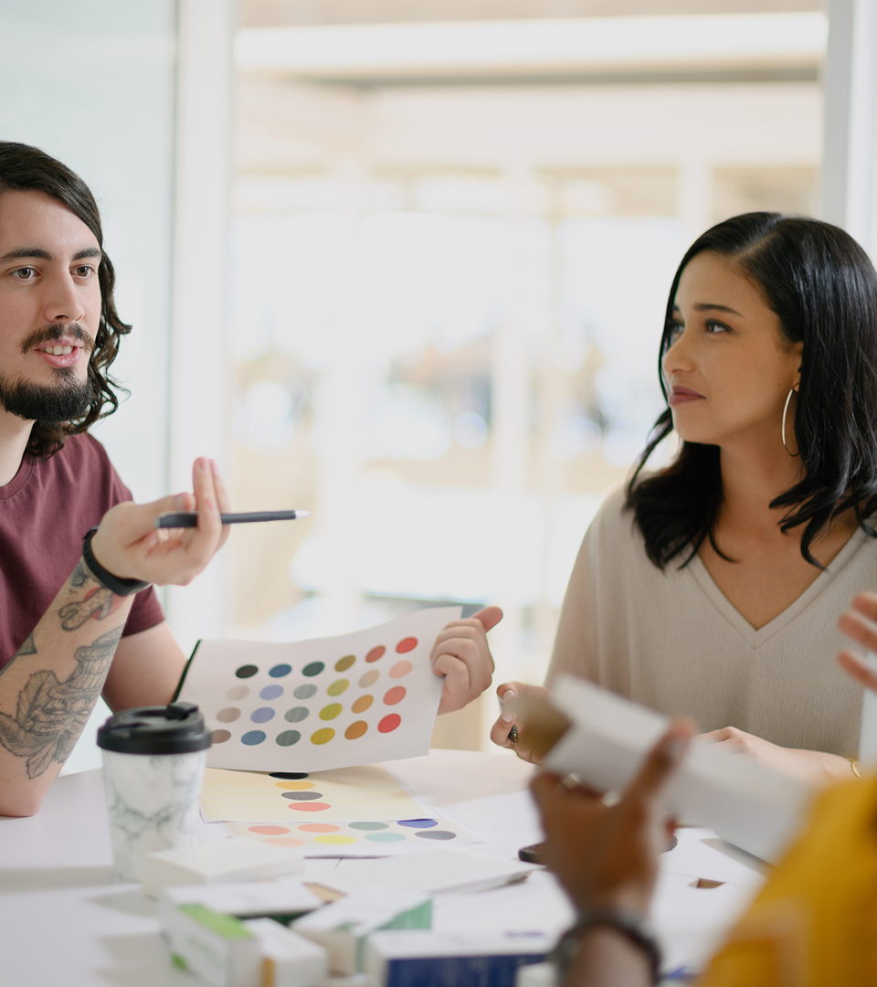 Three colleagues discussing colour palette options during a creative meeting at a bright, modern office table.