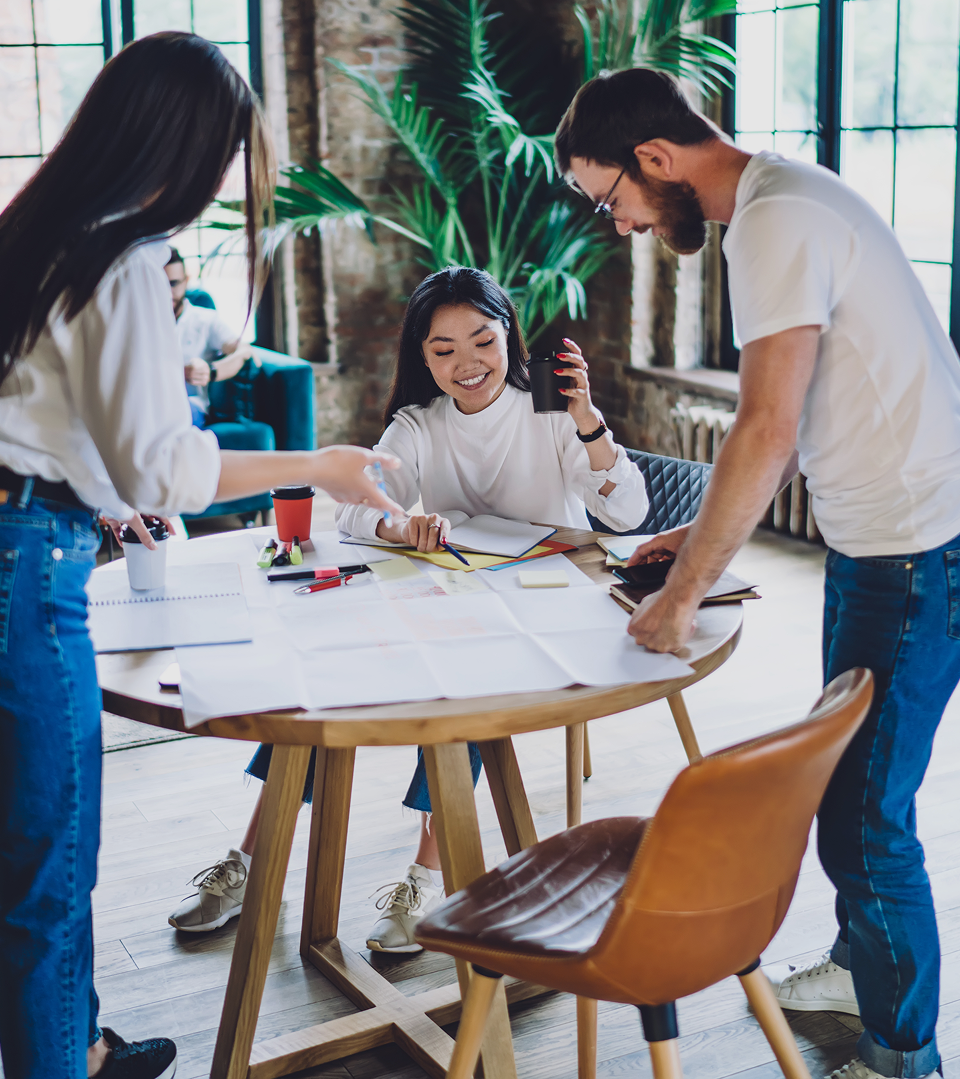 Four people in discussion at a round table in an industrial-style office with exposed brick and natural light.