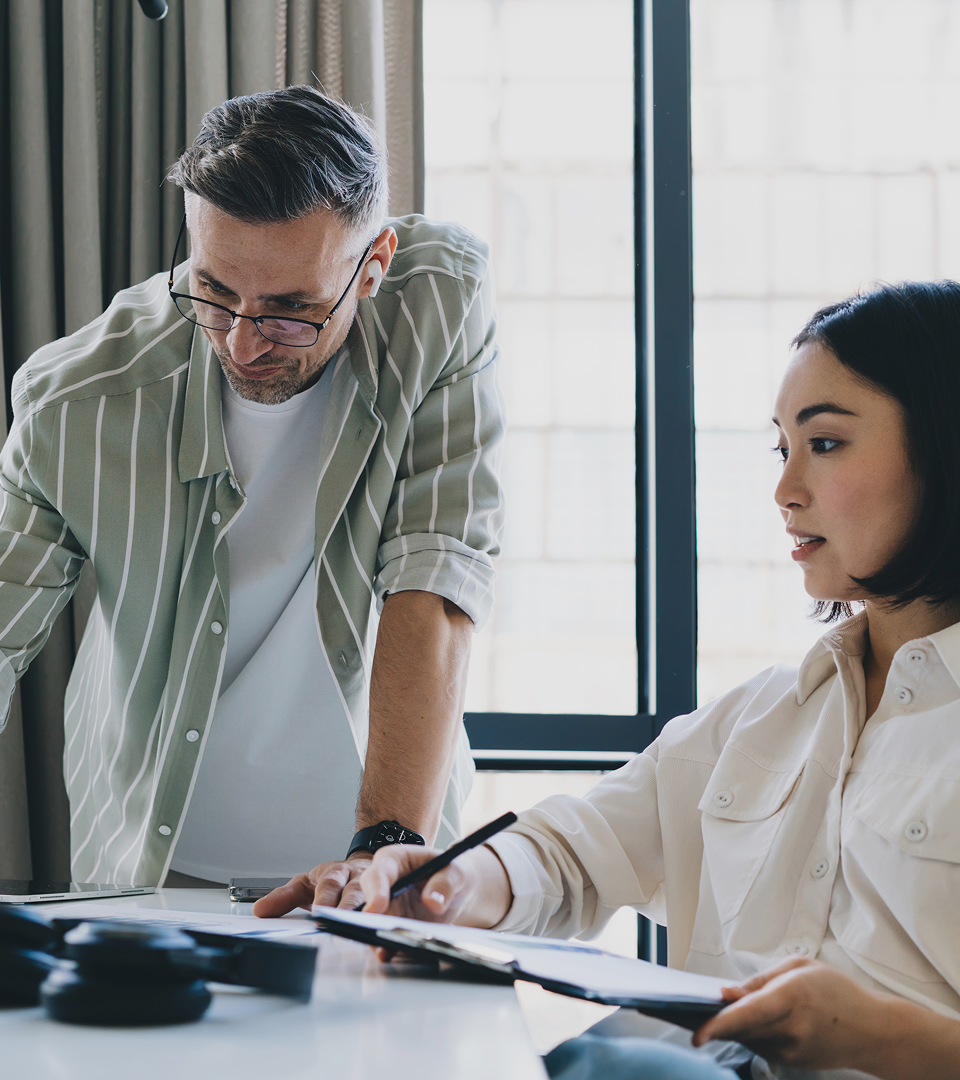 Three colleagues collaborating around a table with papers, notebooks, and coffee cups in a modern, loft-style office.