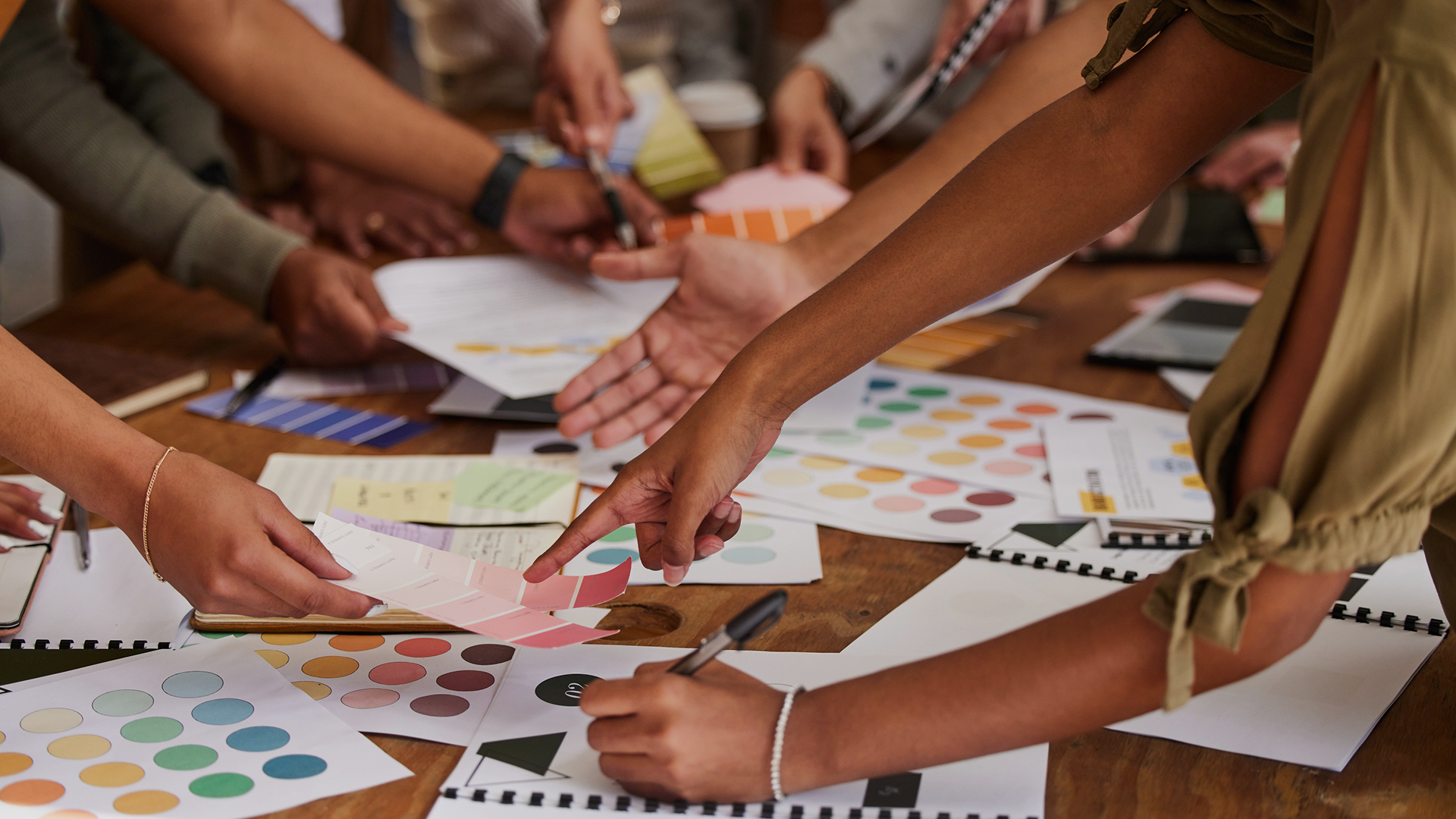 Three colleagues standing together in an office space, reviewing printed materials and discussing ideas around a table.