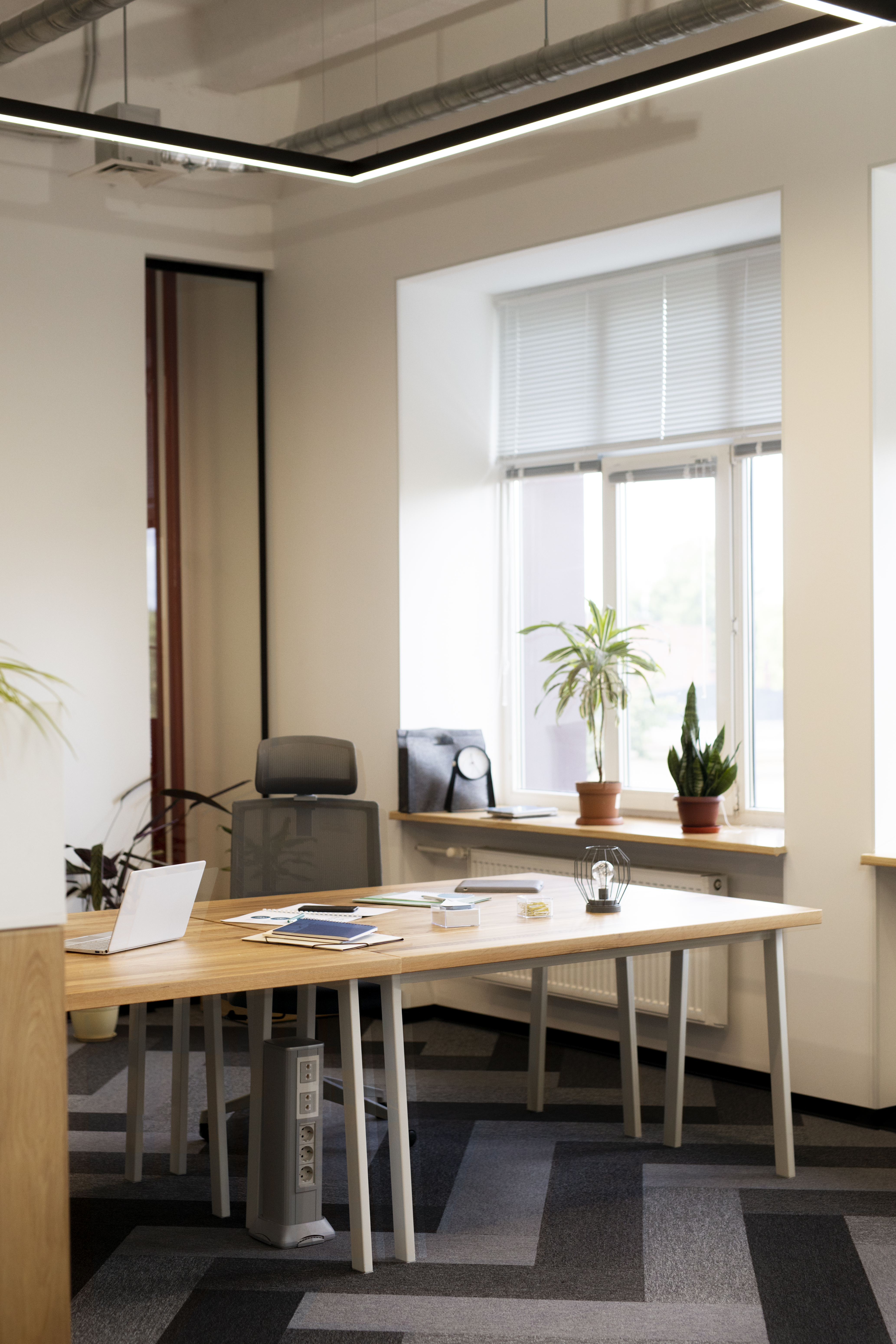 Smiling man standing confidently with arms crossed in a modern office, with colleagues and a meeting room in the background.