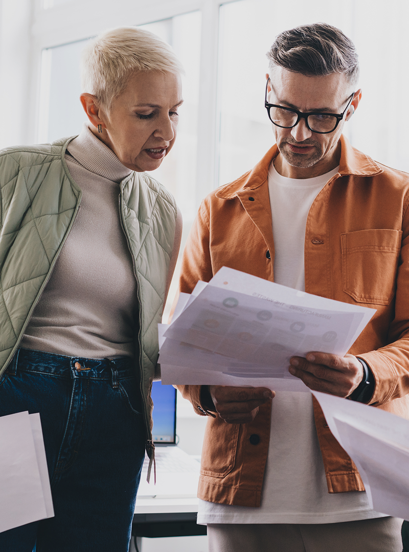 Two team members standingin a bright office, analysing printed charts and documents during a collaborative work session.