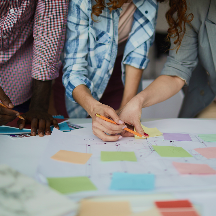 Team collaborating over a layout covered in pastel sticky notes and colour samples, sketching ideas and refining design plans together.
